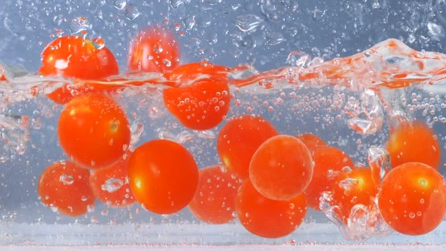 Ripe tasty tomatoes falling in water with big splashing. Slow motion.