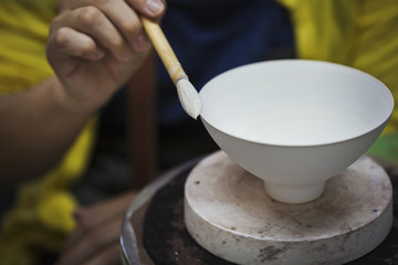 Close up of person working in a Japanese porcelain workshop, glazing white bowls with paintbrush.