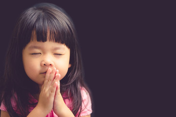 Little girl praying in the morning.Little asian girl hand praying,Hands folded in prayer concept for faith,spirituality and religion.Black background.