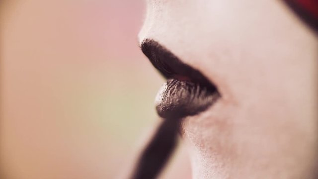 Extreme close up of the female lips. Face art. Professional makeup artist applying black color on the model's lips with special pencil