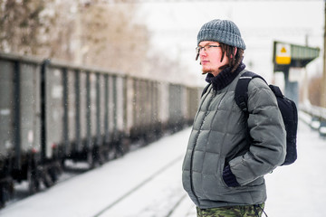 man is waiting for a train at the railway station outdoors in snow in winter