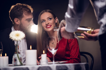 waiter pouring wine while happy couple having romantic date in restaurant on valentines day