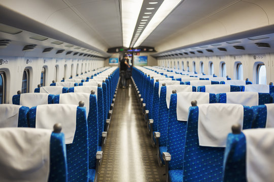 Interior view of passenger train carriage with blue seats, people in the background.