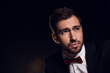 Fototapeta premium sad bearded handsome man in jacket and bow tie, isolated on black
