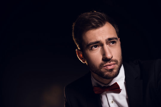 sad bearded handsome man in jacket and bow tie, isolated on black