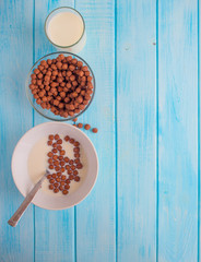milk into chocolate cereal balls in white bowl for breakfast on wooden table
