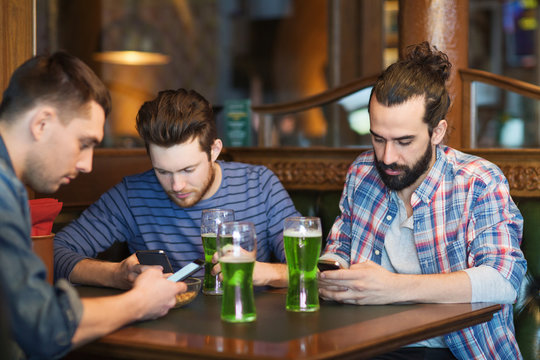 friends with smartphones and green beer at pub