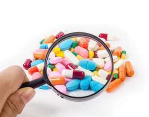 Hand holding magnifying glass with medicine pills.