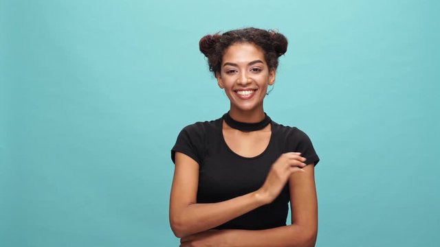 Happy african woman in t-shirt showing peace gestures and waving at camera over blue background