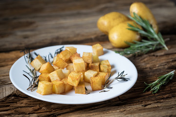 roasted diced potatoes with rosemary and olive oil on the plate on wooden background