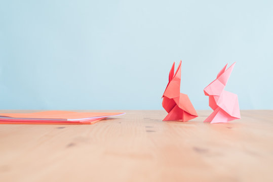 pink and red origami paper bunnies on a wooden table. origami papers on the side