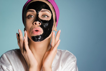 a funny young girl with a pink towel on her head wants to look good, puts a black cleansing mask on her face