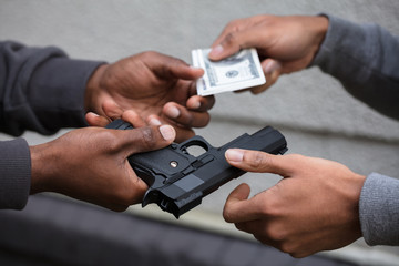 Hands Exchanging Handgun For Banknote