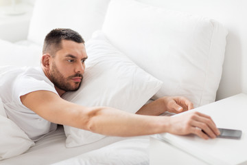 young man reaching for smartphone in bed