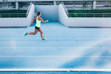 Female caucasian athlete running on blue running track