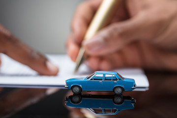 Person's Hand Signing Car Loan Agreement Contract