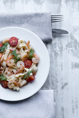 Delicious carbonara with tasty pawns and arugula in a white plate on grey wooden background.
