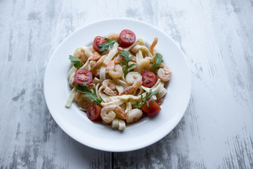 Delicious carbonara with tasty pawns and arugula in a white plate on grey wooden background.