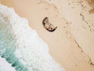 Beach of Bali island with wreckage of the ship. Azure water and waves. Shooting from the sky.