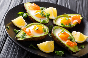 Baked avocado with egg, smoked salmon and greens close-up on a plate on a table. horizontal