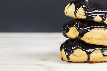 Delicious eclairs in the dripping chocolate glaze on a wooden table.