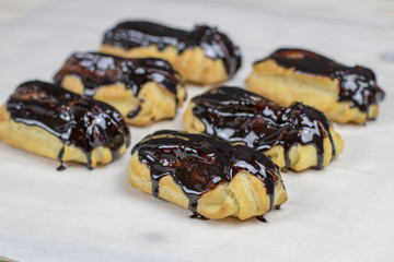 Delicious eclairs in the dripping chocolate glaze on a wooden table.