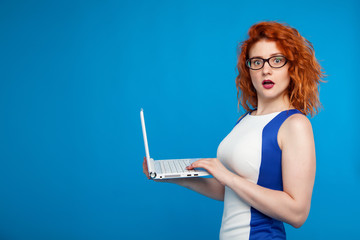 Isolated portrait of a business girl holding a laptop. on a blue background. The girl looks surprised and confused. Place for text. Business and emotional concept