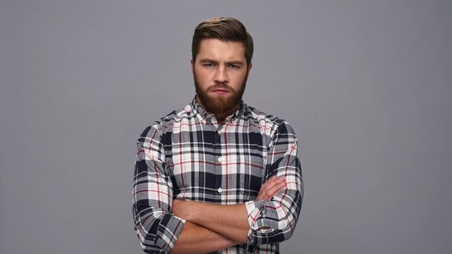 Serious bearded man in shirt looking at the camera with crossed arms over gray background
