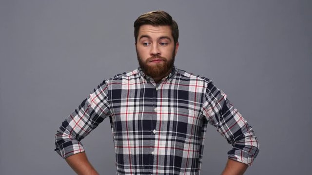 Bored bearded man in shirt with crossed arms looking at the camera over gray background