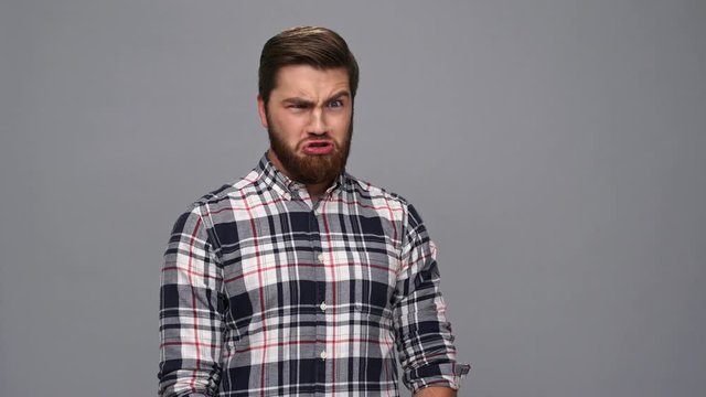 Funny bearded man in shirt showing grimaces and looking at the camera over gray background