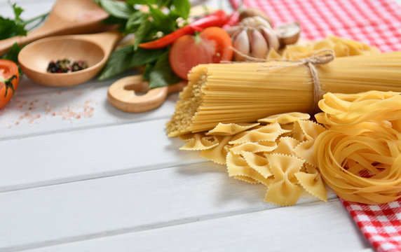 Pasta spaghetti, farfalle, linguine with vegetables and spices on white wooden table