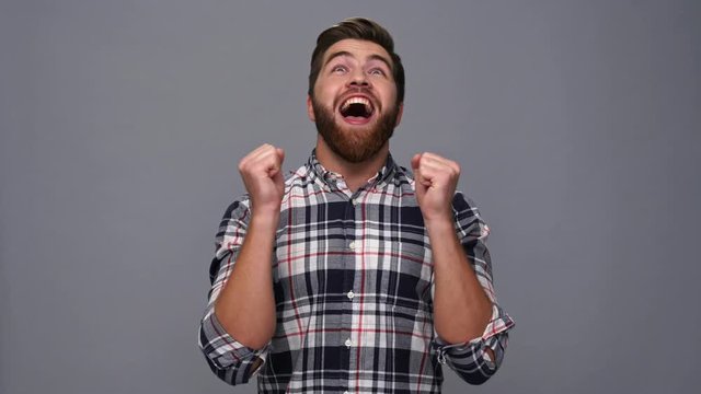 Surprised bearded man in shirt rejoice and screaming over gray background
