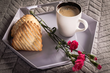 Tray with coffee, flower and cookie with apple, is lay on soft overlay on bed.
