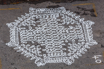Unidentified indian woman seen drawing kolam (in tamil language) or rangoli using white colored rice during festival season