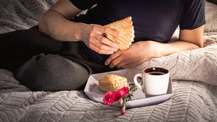 Man in tracksuit sitting on bed and drinking coffee and eat cookie with apple. Photography with vintage filter.