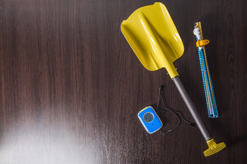 Avalanche rescue kit with probe, detector and shovel lay on wooden background.