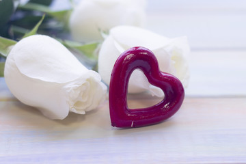 The concept of Love, Wedding, Proposal, Anniversary, St. Valentine's Day, Mother's Day with beautiful white roses and decorative heart in a close up, light wooden background