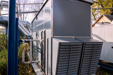 Perspective view of the gray industrial central conditioner standing outdoor on the ground covered by fallen leaves