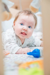 The baby lies in his crib with toys.