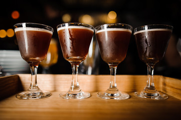 four glasses with chocolate-colored alcoholic cocktails and white foam