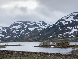 Norwegische Blockh&uuml;tte am See vor Berglandschaft mit Schnee