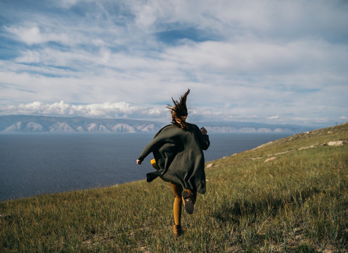 Asian Girl In Sportswear Running Across Field, Morning Workout. Eastern Girl Doing Sports. Side View Of Active Athletic Young Woman Running On Blue Sky Background. Photo With Copy Space