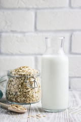 Homemade oat milk in bottle, flour and rolled oats in glass jar on white background. Selective focus, space for text.