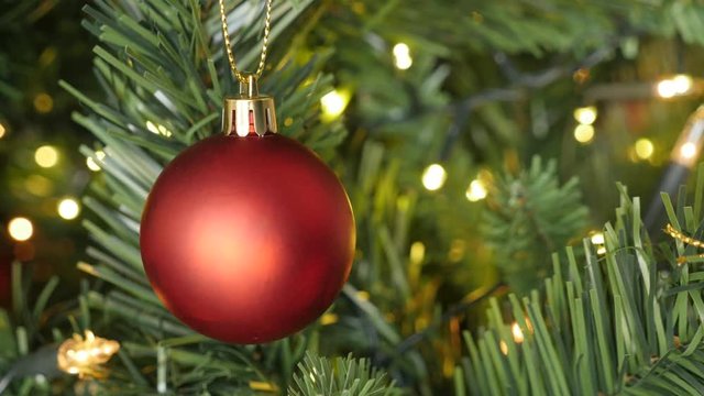 Shiny fairy-lights and bauble on the artificial tree close-up footage - Matte red color Christmas ornament