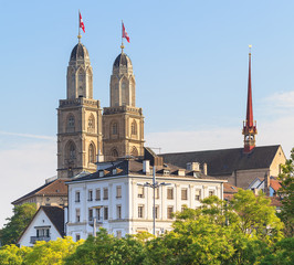View in the city of Zurich, Switzerland - old town buildings and towers of the Grossmunster cathedral decorated with flags of Switzerland