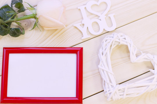 Concept of St.Valentine's Day, Love, Anniversary, Wedding with a pale cream rose, I love you inscription and a red photo frame, natural wooden background, top view
