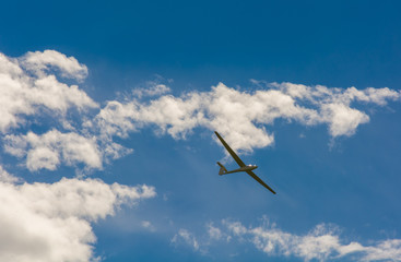 A Glider flying in bleu sky with big white clouds. The glider is a plane that has no engine