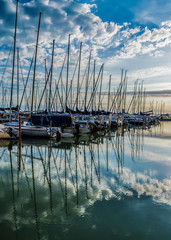 Calm lake, harbor and pier at sunrise. Harbor with sailing boats and pier at dawn with dramatic clouds reflected in water, Lake Balaton, Hungary.