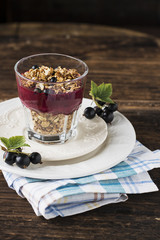 A fine homemade breakfast of granola and berry currant puree from fresh garden organic berries in a simple glass serving glass on a dark wooden background full of vitamin C. Selective focus.