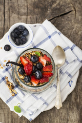 A healthy breakfast snack from granola, vanilla chia pudding, strawberries, blueberries in a large serving glass on a simple wooden background. The concept of healthy eating. Selective focus.